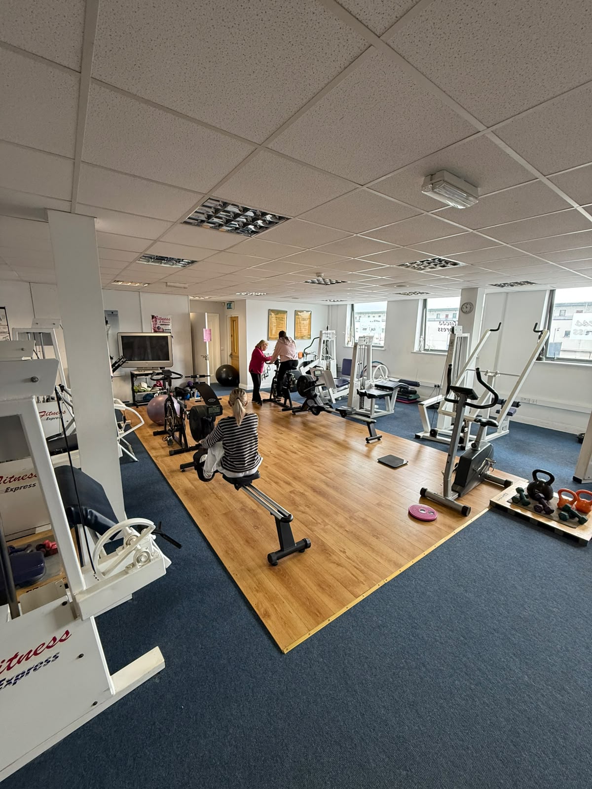 A Fitness Express coach helping a member on the exercise bike while another member rows